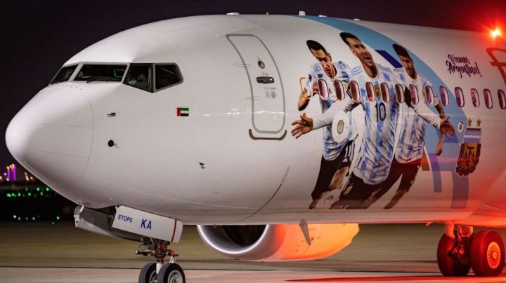 Members of the Argentinian team peer out from the windows on their plane adorned with a picture of Argentina's forward Lionel Messi and teammates as the team arrives at the Hamad International Airport in Doha on November 17, 2022, ahead of the Qatar 2022 World Cup football tournament. (Photo by Odd ANDERSEN / AFP) (Photo by ODD ANDERSEN/AFP via Getty Images)