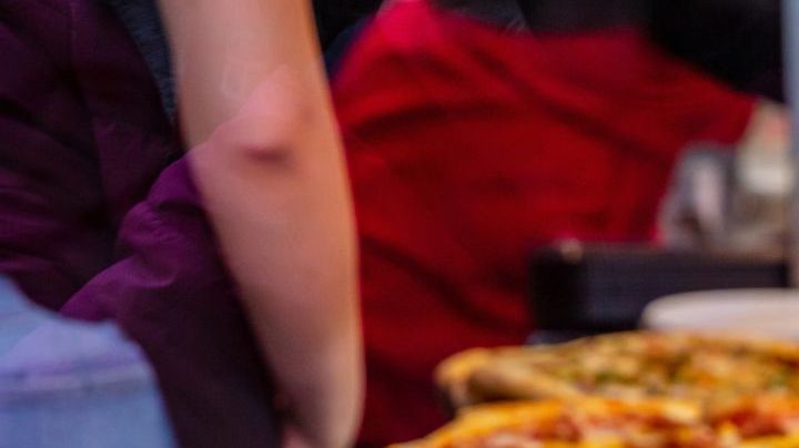 Pizzeria glass window. Variety of italian pizzas in a shop display, street food. Kitchen workers arranging the pizzas.