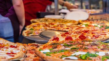 Pizzeria glass window. Variety of italian pizzas in a shop display, street food. Kitchen workers arranging the pizzas.