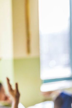 Back view of large group of elementary students raising hands to answer teacher's question on a class at school. Focus is on black girl.