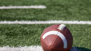 American football ball at yard line markers on playing field - stock photo