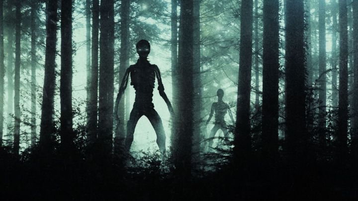 Horror, sci fi concept of aliens standing in a forest. Silhouetted by bright UFO lights at night