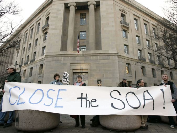 WASHINGTON - FEBRUARY 22: Protesters hold a banner during a demonstration February 22, 2005 outside the Justice Department in Washington, DC. Protesters called on the resignation of recently appointed U.S. Attorney General Alberto Gonzalez and the closure of the School of the Americas, a combat training school for Latin American security personnel that was found teaching torture techniques and was later renamed as the Western Hemisphere Institute for Security Cooperation, in 2001. (Photo by Alex Wong/Getty Images)