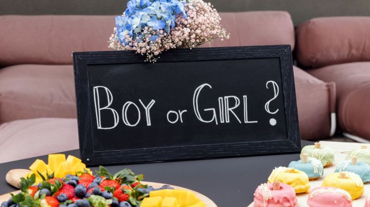 Beautifully set table for a gender reveal party at a rooftop terrace. There are no people since the guests haven't arrived yet. The table is full of delicious sweets and snacks that are waiting for the guests.