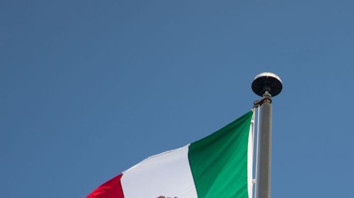Bottom View of Passenger Airplane Flying Over Waving Mexico Flag On Pole.