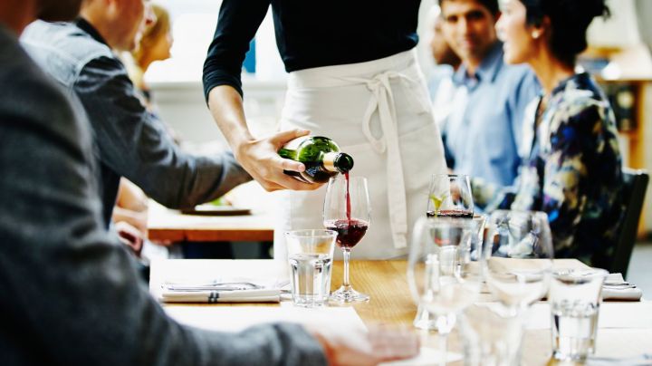 Waitress pouring wine into glass at table in restaurant