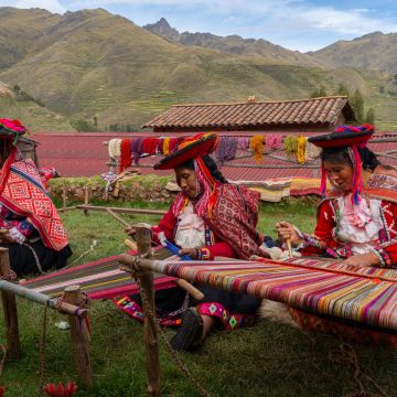 Three local female weavers in colourful traditional local dress including festooned hats, weaving colourful alpaca wool on the ground, Chumbe Community, Lamay, Sacred Valley, Peru (3 Model Releases and Property Release) - stock photo