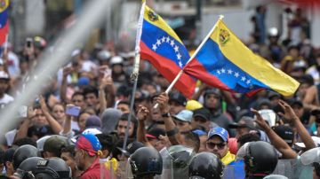 Police officers stand guard next to demonstrators waving Venezuelan flags during a protest against Venezuelan President Nicolas Maduro's government in Caracas on July 29, 2024, a day after the Venezuelan presidential election. Protests erupted in parts of Caracas Monday against the re-election victory claimed by Venezuelan President Nicolas Maduro but disputed by the opposition and questioned internationally, AFP journalists observed. (Photo by Yuri CORTEZ / AFP) (Photo by YURI CORTEZ/AFP via Getty Images)