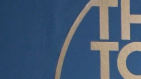 Amaya and Bryan from Love Island USA Season 7 wearing all black and standing next in front of a blue background with the logo for "The Tonight Show starring Jimmy Fallon" in gold lettering