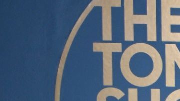 Amaya and Bryan from Love Island USA Season 7 wearing all black and standing next in front of a blue background with the logo for "The Tonight Show starring Jimmy Fallon" in gold lettering