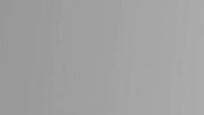 Vero Rodriguez in red dress with her hands splayed to the side of her head with a grey background