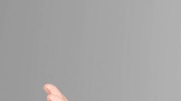 Vero Rodriguez in red dress with her hands splayed to the side of her head with a grey background